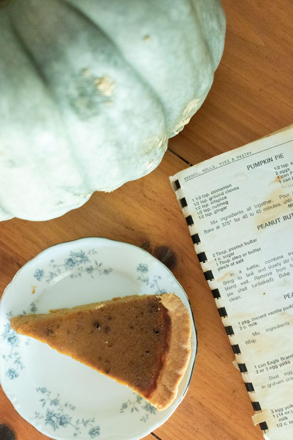 green jarahdel pumpkin, old community cookbook and a slice of pumpkin pie on a blue floral plate