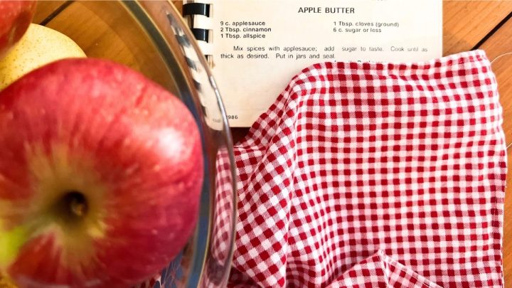 apples in a bowl next to an old community cookbook with apple butter recipe
