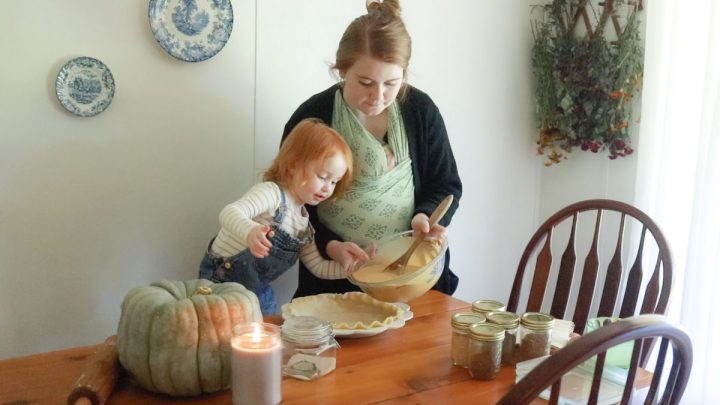 redhead toddler and woman in black sweater and green baby wrap pour pumpkin pie filling into pie shell