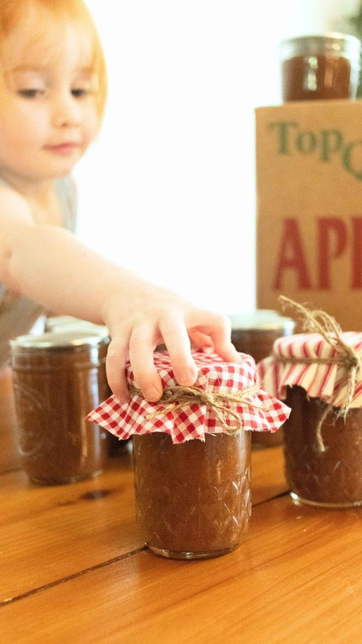 redhead toddler girl reaching for a half pint jar of apple butter