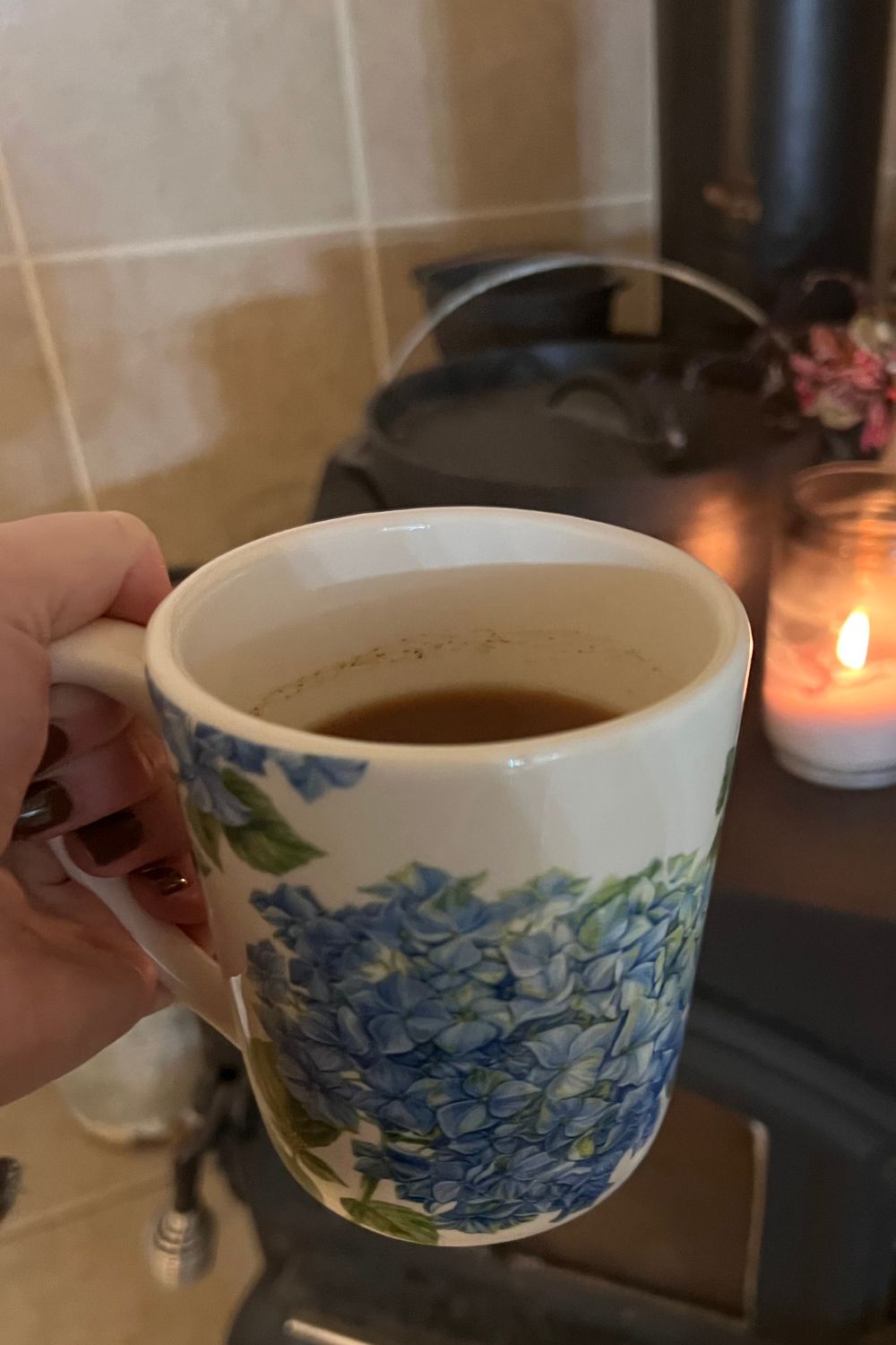 old fashioned apple cider in a hydrangea mug held in front of wood burning stove